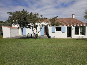 A white building with a tiled roof, a tree in the yard, and a table with chairs.