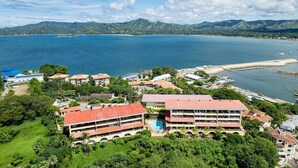 A coastal resort with multiple buildings, a swimming pool, and a view of the sea and mountains. - 5mins to Marina-Oceanview-Full Kitchen-Pool-AC-Gym – Presidential Suites 4 (Playa Flamingo)