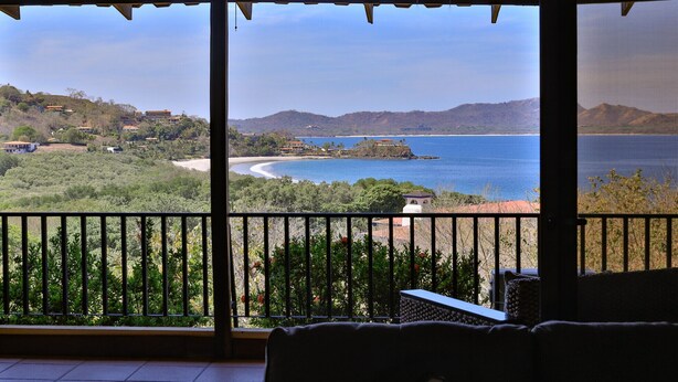 A balcony with a view of a coastal landscape, including a beach and distant hills. - 5mins to Marina-Oceanview-Full Kitchen-Pool-AC-Gym – Presidential Suites 4 (Playa Flamingo)