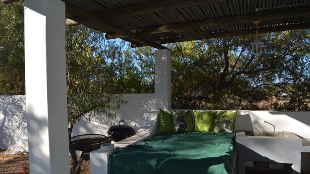 Patio esterno con barbecue, tavolo con tovaglia verde e parete bianca.