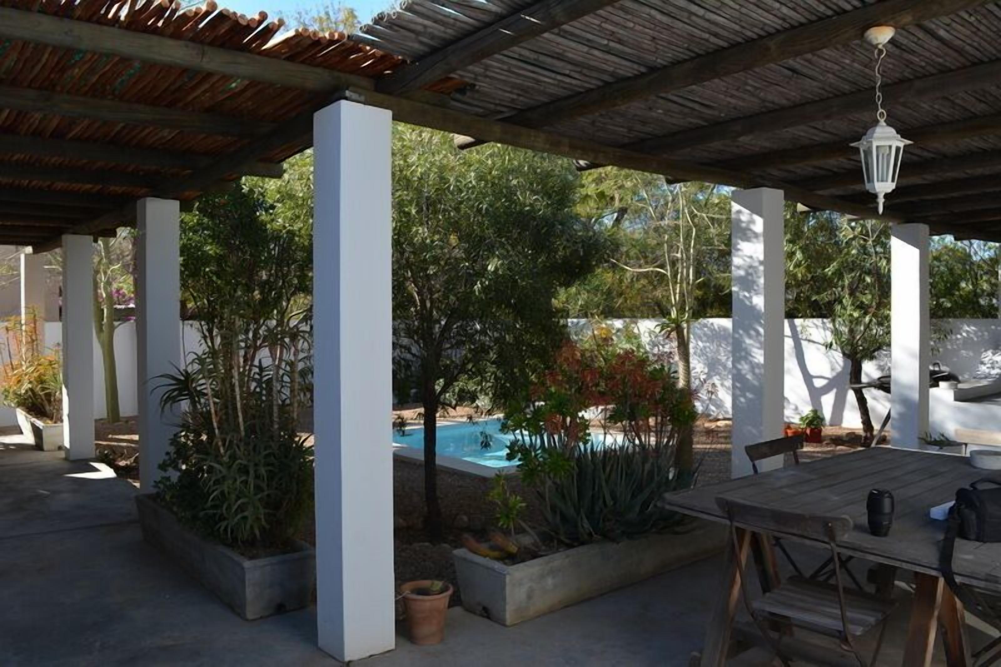 An outdoor patio with a pool, surrounded by planters and a wooden table.