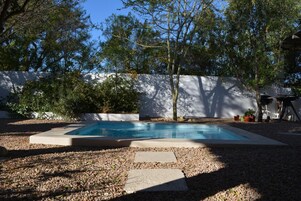 Piscina rectangular con solárium de hormigón, rodeada de grava y árboles.