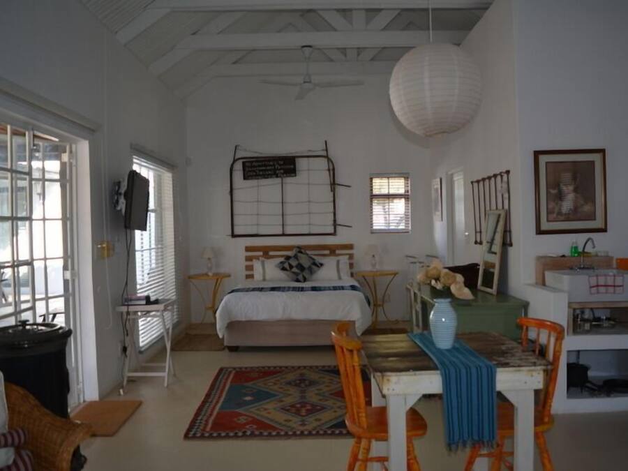 A bedroom with a bed, bedside tables, a desk, a chair, a rug, and a hanging light fixture.