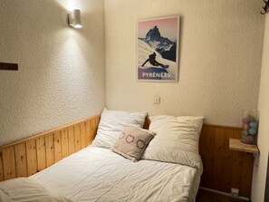 A bedroom with a wooden headboard, white bedding, and a poster of a mountain scene.