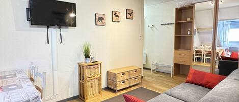A modern living room with a sofa, a television mounted on the wall, a small side table with a plant, and a wooden cabinet.