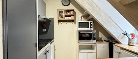 Eine kompakte Küche mit integriertem Mikrowellenherd, einem kleinen Backofen und einer Wanduhr.