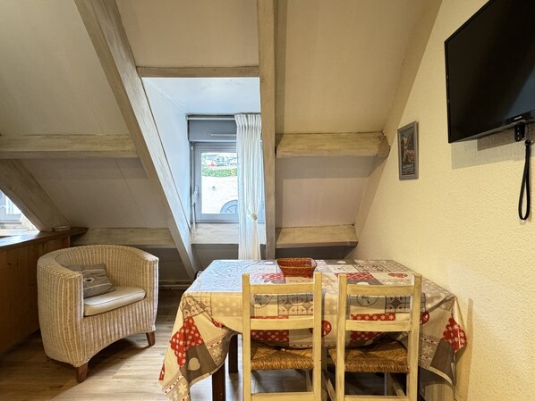 Un coin repas accueillant avec une table dressée pour deux personnes, une chaise en osier et un téléviseur fixé au mur.
