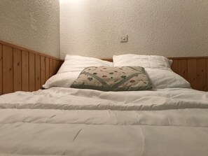 Un lit avec une literie blanche, un coussin à motifs floraux et une tête de lit en bois.