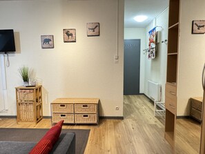 Une pièce avec un plancher en bois, un canapé, un coussin rouge, une petite table avec une plante, des paniers en osier et des œuvres d’art accrochées au mur.