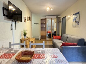 A cozy living room with a grey sofa, a television mounted on the wall, and a small table with a basket.