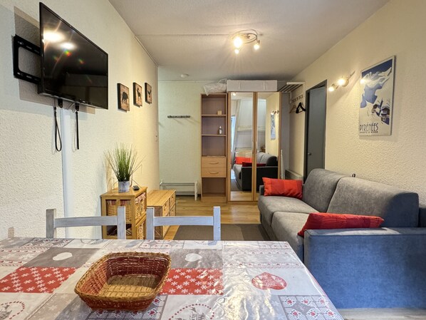 A furnished living room with a television, a sofa, a table with a basket, and a wall-mounted TV.
