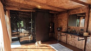 Une pièce rustique avec un plafond en bois, un grand miroir, un lavabo avec une serviette, et un chat sur le sol.
