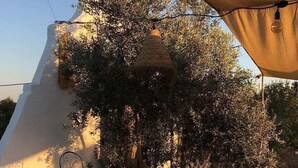 Un espace de restauration en plein air avec une table ronde, deux chaises, un petit tabouret et une lampe décorative suspendue.