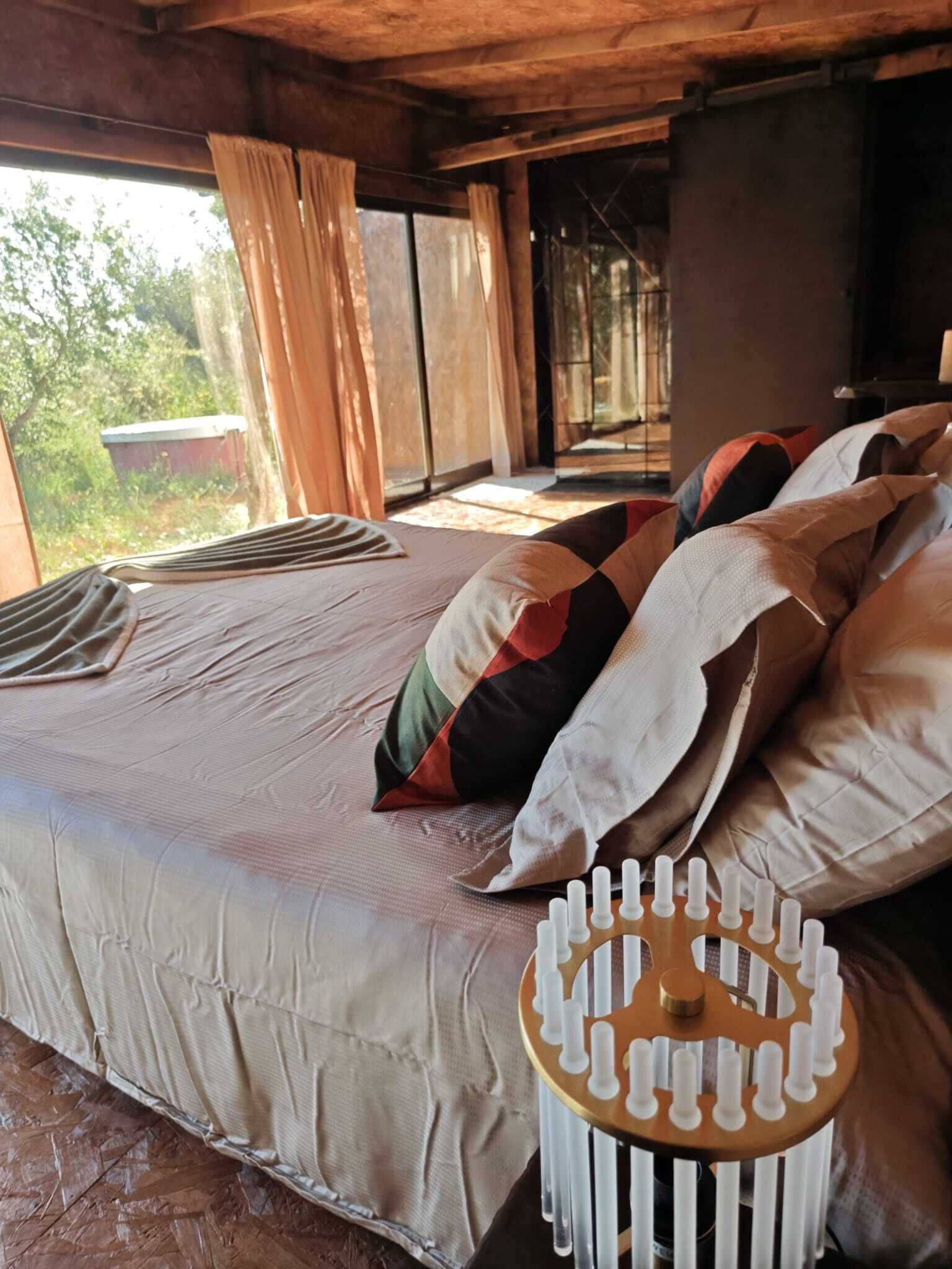 A bed with a patterned blanket and pillows, a wooden headboard, and a view of greenery outside.