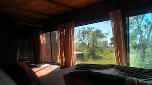 Une chambre avec un lit, une fenêtre avec des rideaux et une vue sur les arbres et la verdure.