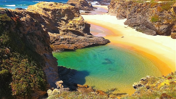 Un paysage côtier avec une plage, des falaises rocheuses et une eau d’un bleu limpide.