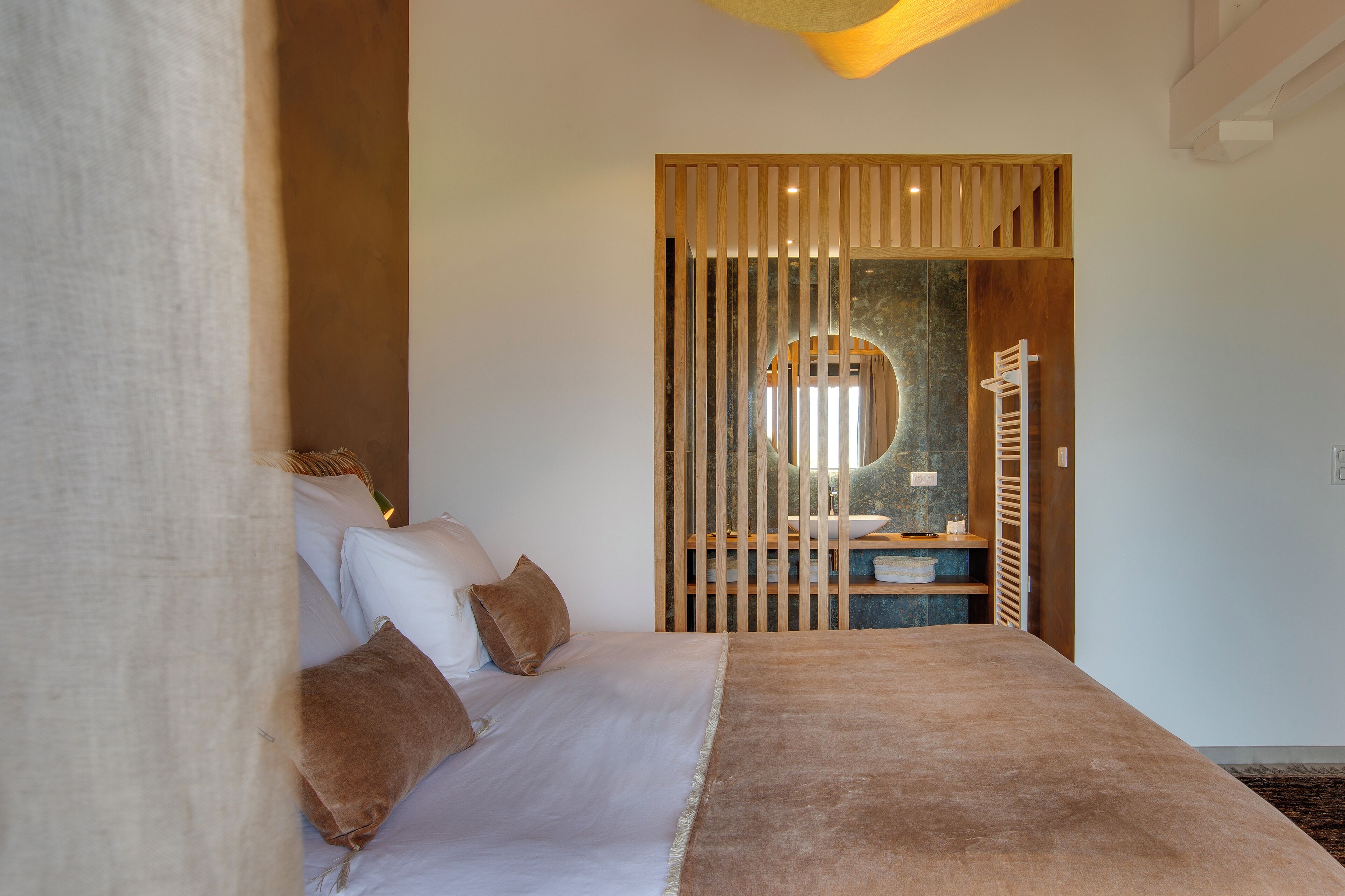A bedroom with a bed, pillows, a wooden partition, and a bathroom visible through the partition.