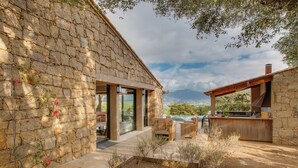 A stone building with a patio area, outdoor seating, and a view of the landscape. - Magnificent villa of 260m2 air-conditioned sea view heated swimming pool and beach on foot (Olmeto)