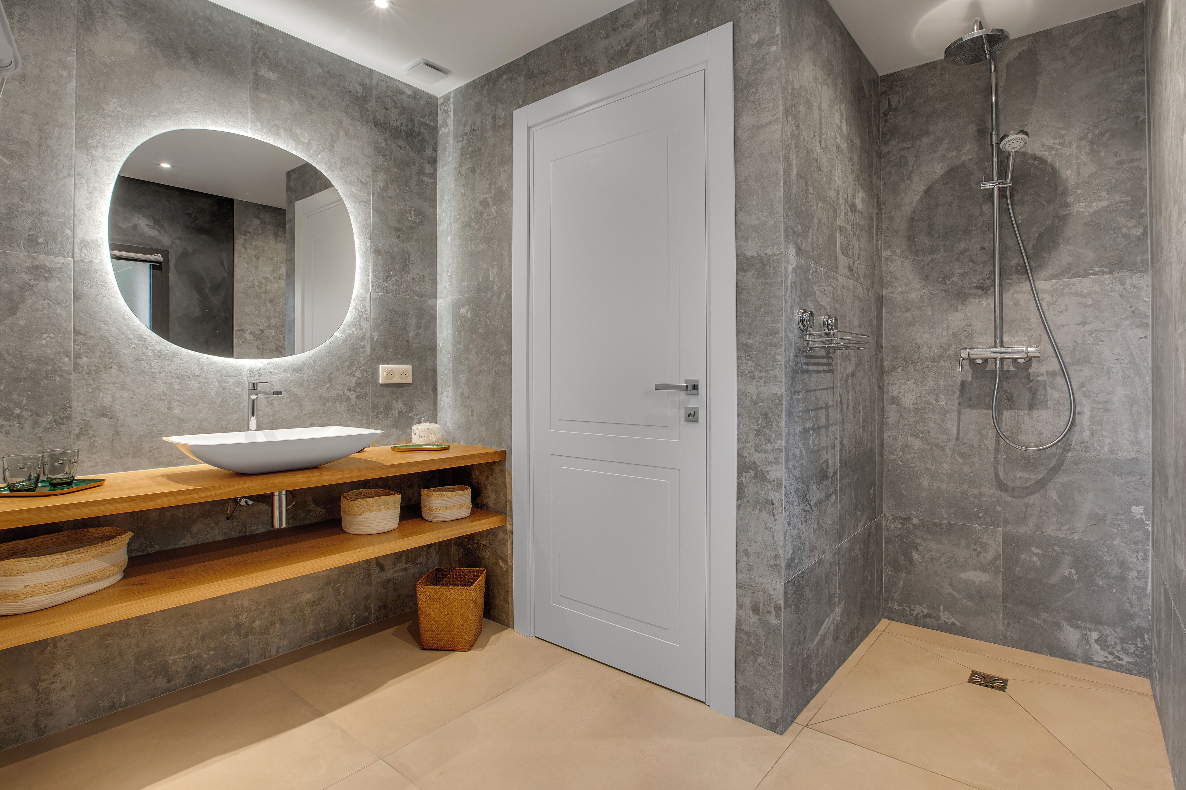 A modern bathroom with a large mirror, a vessel sink, wooden shelves, and a shower area.