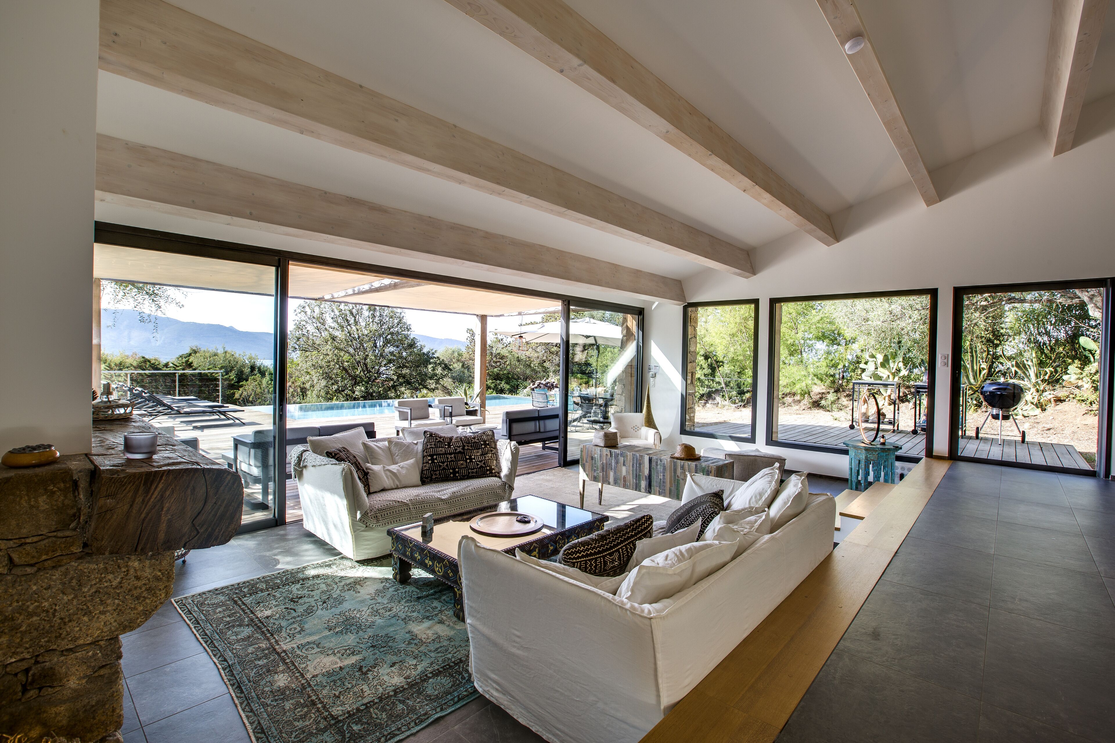 A spacious living area with a large sofa, coffee table, and a view of a pool and mountains.