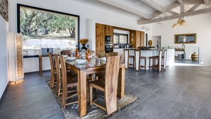 A spacious dining area with a large wooden table and chairs, a kitchen in the background, and a view of the outdoors through large windows. - Magnificent villa of 260m2 air-conditioned sea view heated swimming pool and beach on foot (Olmeto)