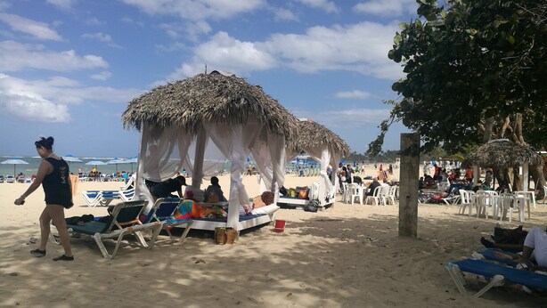 Une plage avec des cabanes à toit de chaume, des chaises longues et des parasols.