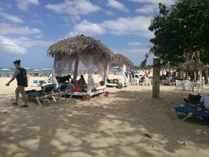 A beach with thatched-roof huts, lounge chairs, and umbrellas.