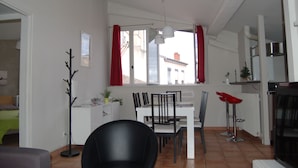 A dining area with a white table, black chairs, and a red curtain. There is a black floor lamp and a white cabinet with a plant.