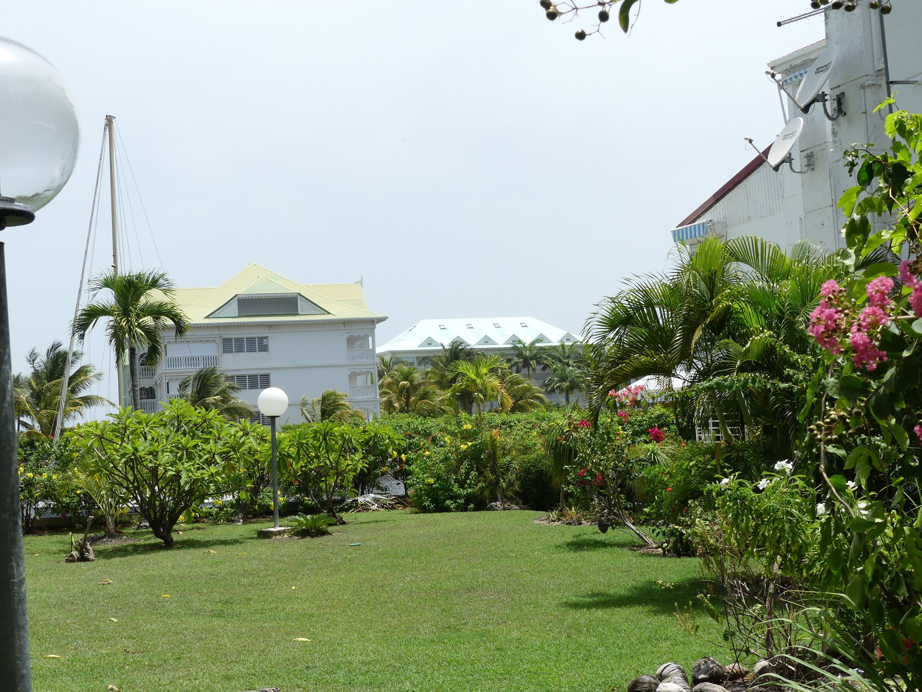 A lush garden with a variety of plants and flowers, a well-maintained lawn, and a building with a distinctive green roof in the background.
