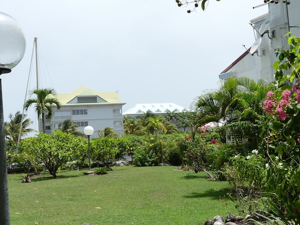 A lush garden with a variety of plants and flowers, a well-maintained lawn, and a building with a distinctive green roof in the background.