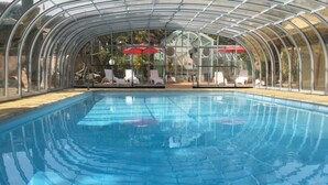Ein Swimmingpool mit Glasdach, Liegestühlen und Sonnenschirmen.