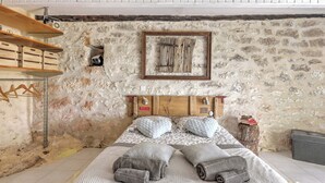 A bedroom with a stone wall, wooden headboard, and a bed with rolled towels. - quercy stone guest rooms decorated with taste. (PORTE-DU-QUERCY)
