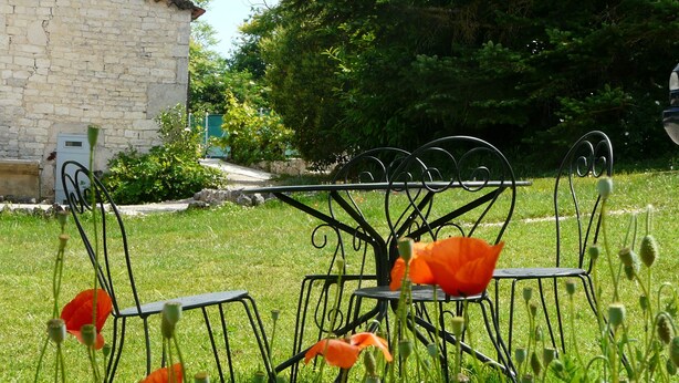 A garden with a metal table and chairs, surrounded by greenery and flowers. - quercy stone guest rooms decorated with taste. (PORTE-DU-QUERCY)