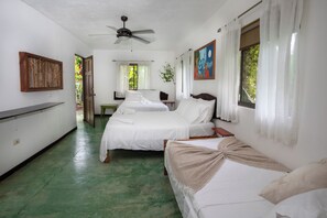 Ein Zimmer mit zwei Betten, einem Deckenventilator, einem Schreibtisch und einem Fenster mit Vorhängen.