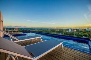 A rooftop infinity pool with lounge chairs, a wooden deck, and a view of the city skyline. - 302 P88-Amazing Apartment 2BedRoom (Playa del Carmen)