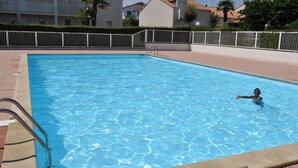 Una piscina rectangular amb aigua blava cristal·lina, envoltada per una tanca blanca i un passeig pavimentat.