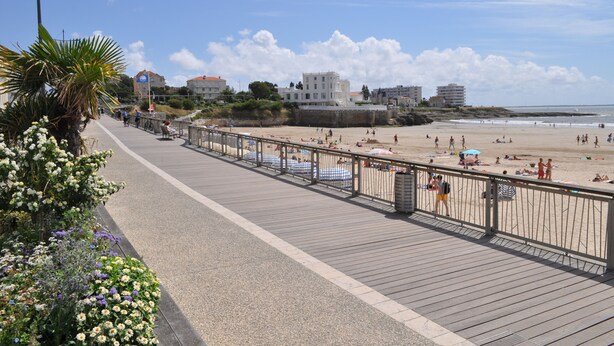 Una passejada marítima amb un camí de fusta, parasols de platja i gent relaxant-se.