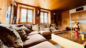 A cozy living room with a brown leather sofa, patterned cushions, a wooden coffee table, and a deer head mounted on the wall. - ✨CHALET WITH A CINEMATIC VIEW  (Ormont-Dessus)