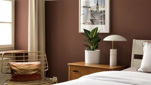 A hotel room with a bed, a bedside table with a lamp, a chair with a cushion, a potted plant, and a framed picture on the wall. - Sunny Old Town Flat •  Walk Everywhere • Sleeps 4 (Bern)