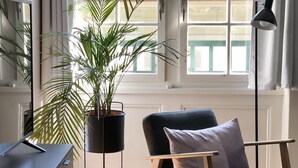 A modern living room with a dark grey armchair, a black floor lamp, a potted plant, and a glass coffee table. - Sunny Old Town Flat •  Walk Everywhere • Sleeps 4 (Bern)
