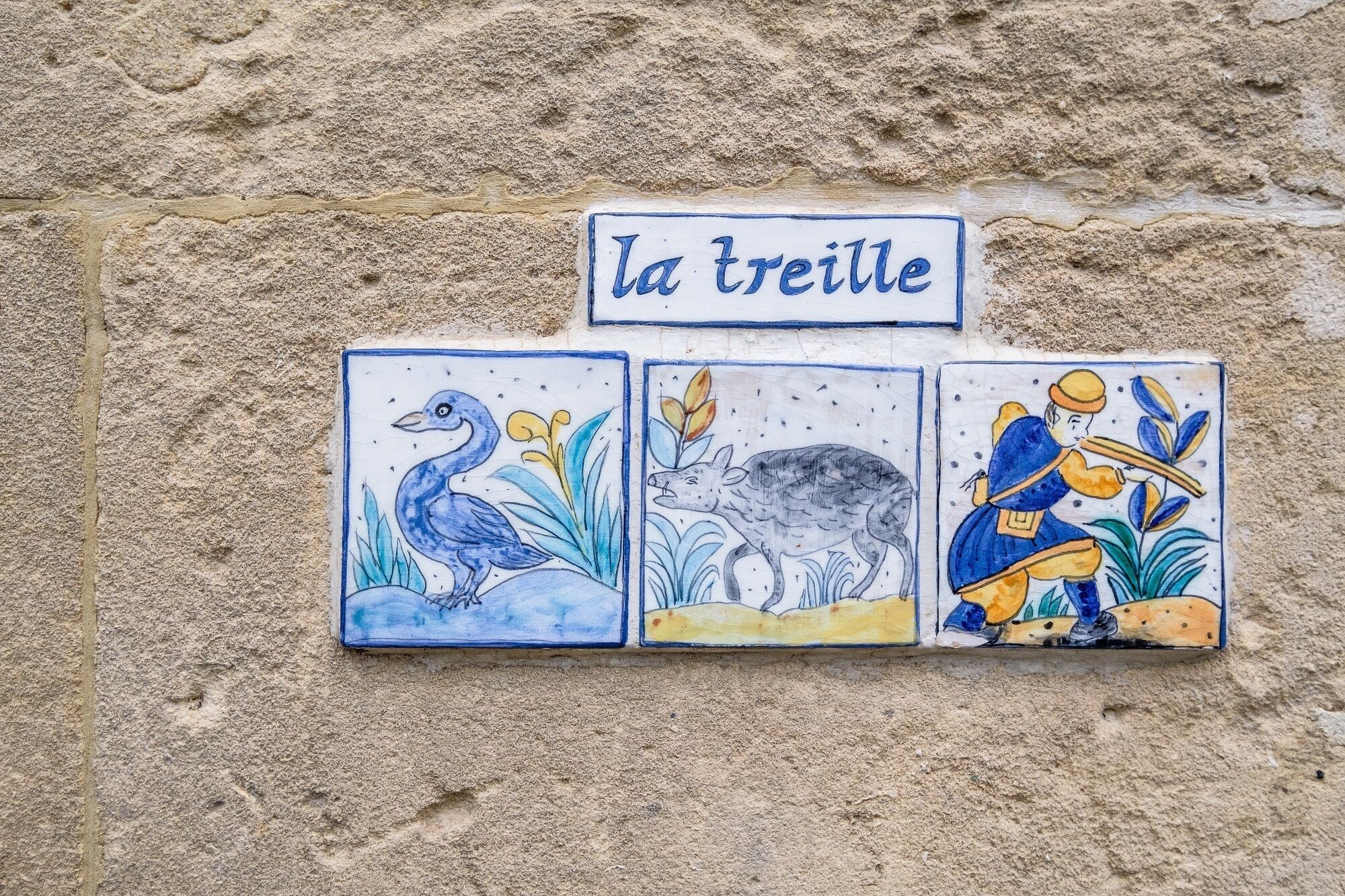 Drie keramische tegels met dierenillustraties en de tekst 'la treille' op een structuurwand.