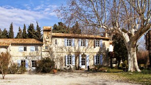 A stone building with a tiled roof, multiple windows, and a large tree in the foreground. - La Treille du Mas Vacation Rental—3-Star Rating (Arles)