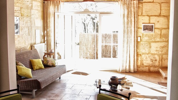 A cozy room with a sofa, a table with books, and a view of the outside. - La Treille du Mas Vacation Rental—3-Star Rating (Arles)
