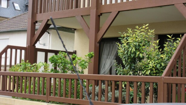 Un balcon avec une balustrade en bois, une fenêtre avec un rideau et une plante en pot.
