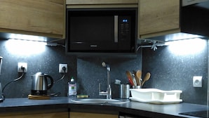 Une cuisine compacte dotée de meubles en bois, d’un four à micro-ondes, d’une bouilloire et d’un lave-vaisselle.