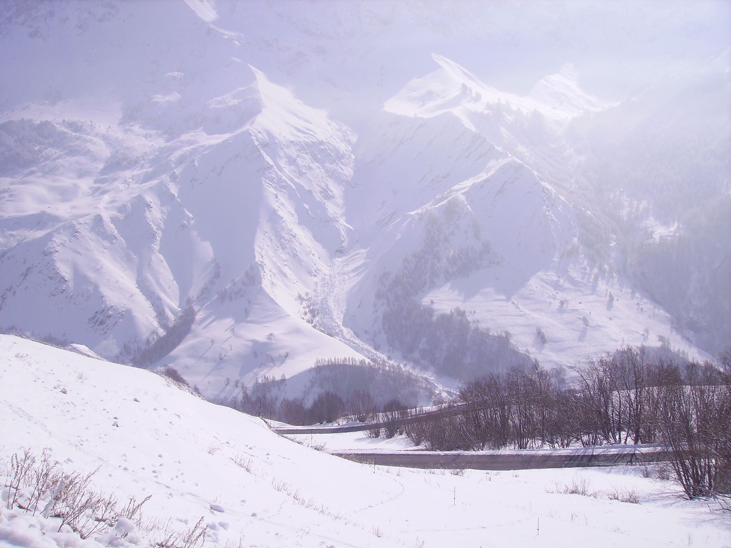 Schnee bedecktes Berglandschaft mit einem Tal und einem Pfad hindurch.