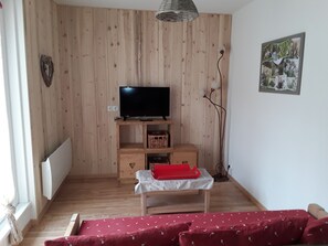 Quarto com parede de madeira, televisão em móvel de madeira, mesinha com tecido vermelho e sofá vermelho.