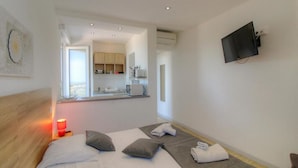 Una habitación de hotel moderna con una cama, un televisor montado en la pared y una kitchenette al fondo.