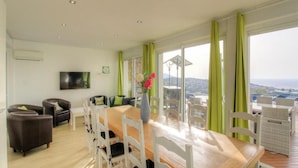Un comedor con una mesa y sillas de madera, un jarrón con flores y vistas amplias por las ventanas.