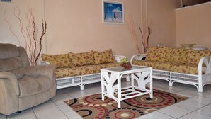 Un salon avec un canapé beige, un fauteuil blanc et une table basse blanche. Un tableau est accroché au mur et un tapis à motifs recouvre le sol.